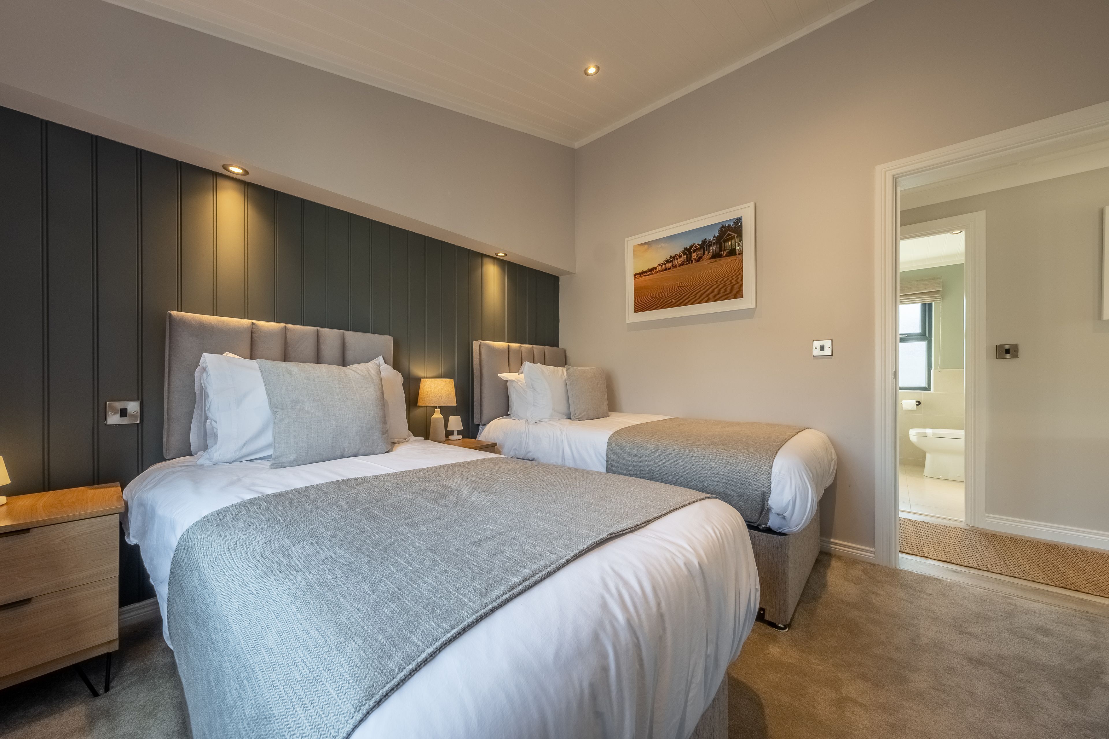 A hotel room with two beds, a nightstand, a lamp, and a painting on the wall.