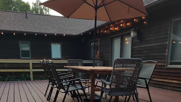 Une terrasse en bois agrémentée d’un foyer à verre, de mobilier d’extérieur et de guirlandes lumineuses.