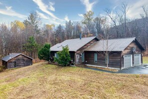A rustic cabin with a sloped roof, a front porch, and a garage. - Expansive mountainside retreat, close to Stowe, Smuggler's Notch, Jay (Morristown)