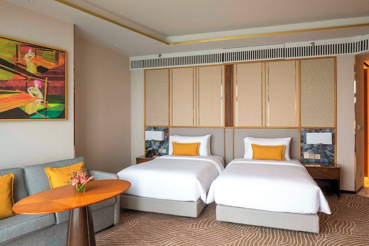 A hotel room with a sofa, two beds, a table, and a painting on the wall.