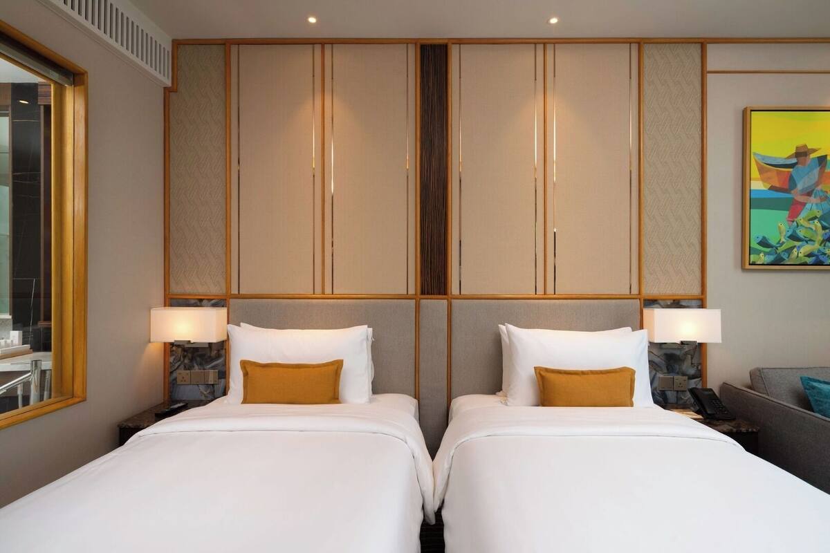A hotel room with two beds, a large mirror, and a painting on the wall.