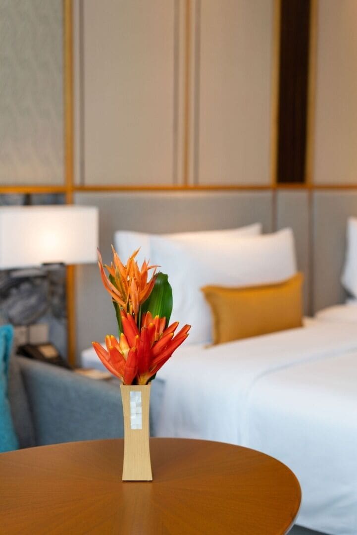 A hotel room with a bed, a bedside table with a vase of flowers, and a lamp.