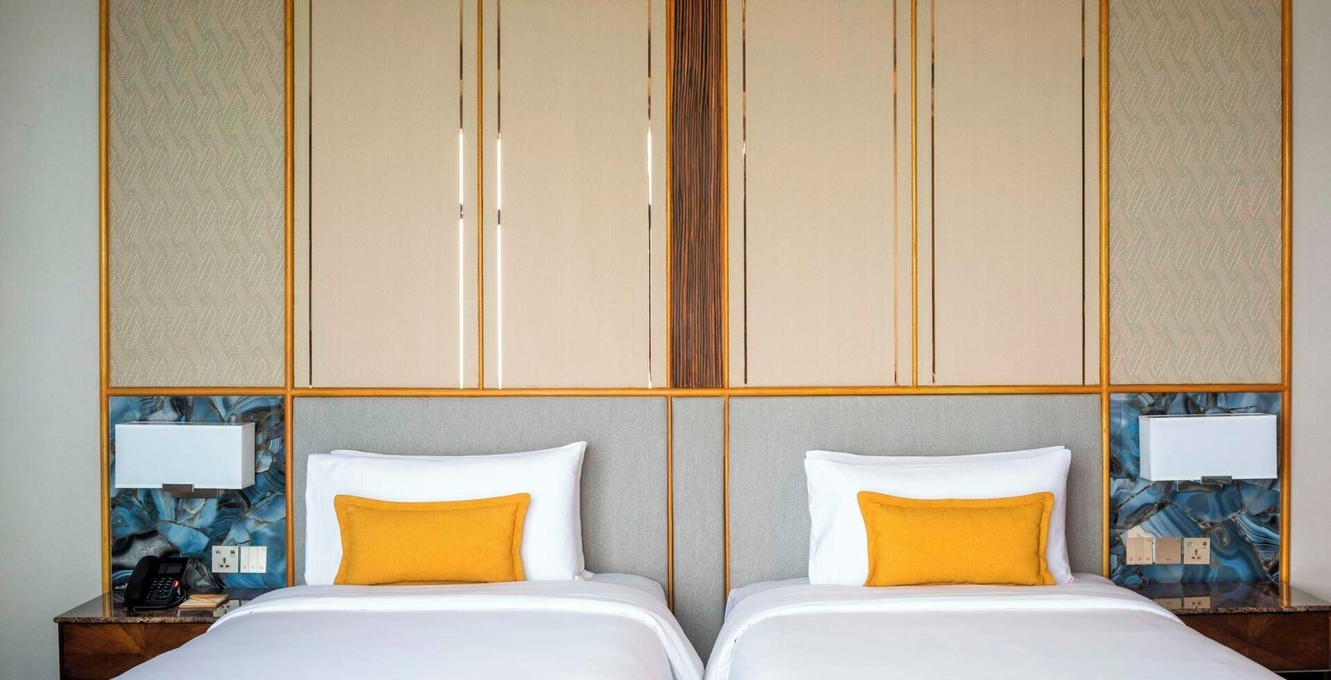 A hotel room with two beds, a minibar, a telephone, and a nightstand with a lamp.