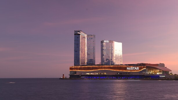 Un hotel frente al agua con un diseño moderno, que presenta dos imponentes edificios altos al fondo y una estructura curva distintiva en primer plano.