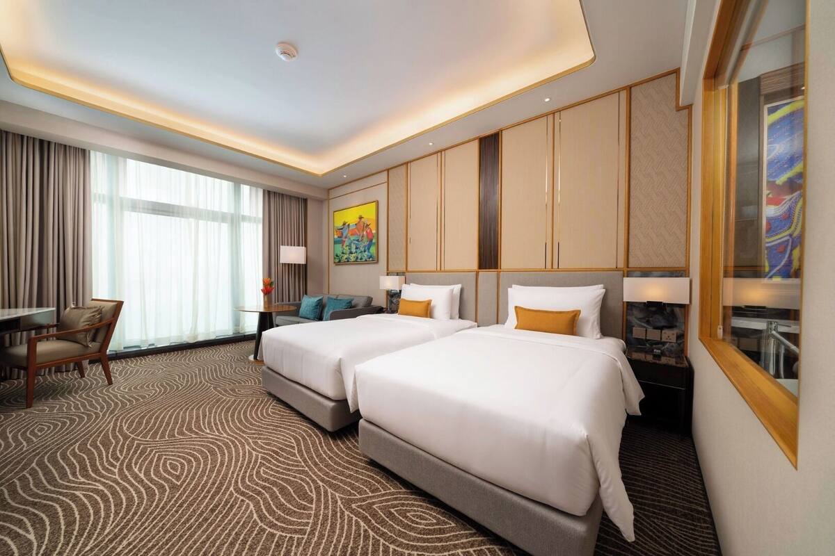 A hotel room with two beds, a desk, a chair, and a large window.