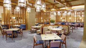 Un restaurante con vigas de madera, mesas redondas y asientos con cojines azules.