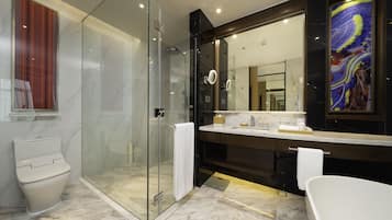 A modern bathroom with a glass-enclosed shower, a white toilet, a large mirror, and a bathtub.