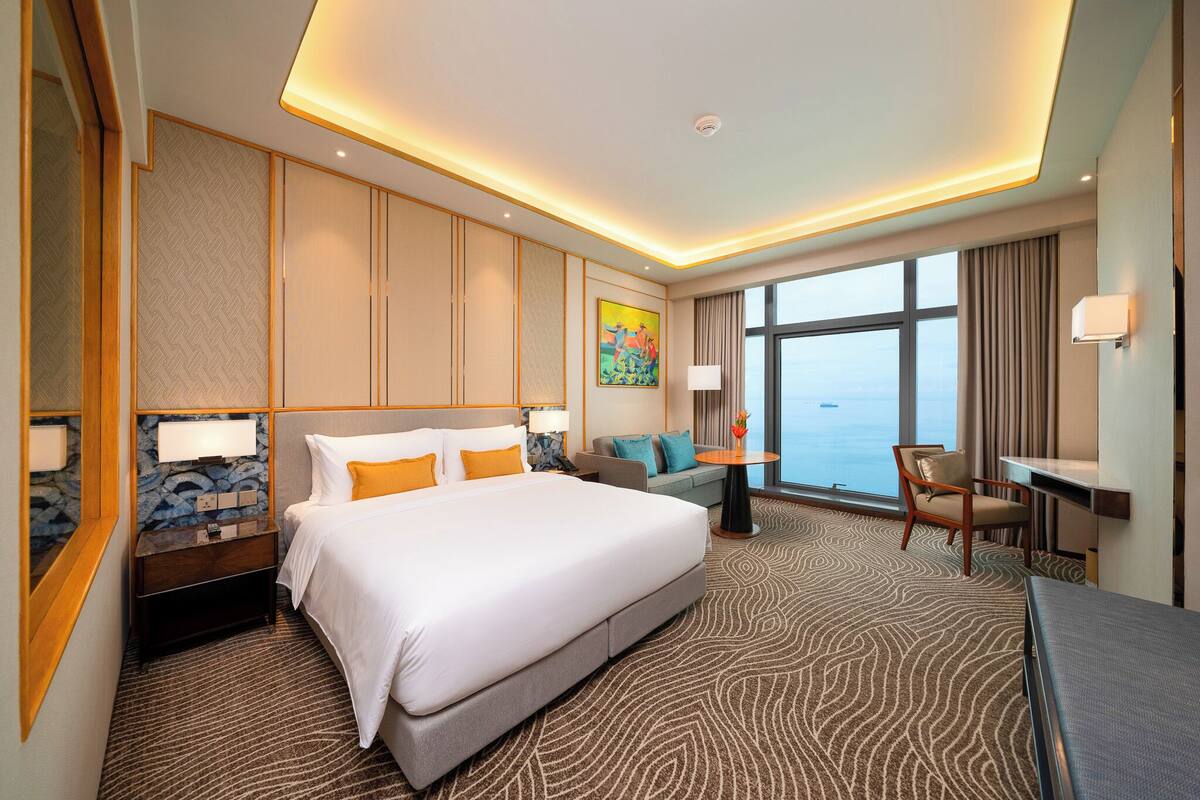 A hotel room with a large bed, a sofa, a desk, and a view of the sea.