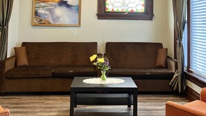 En stue med en brun sofa, et sofabord med en vase blomster, et maleri og et glasmaleri.