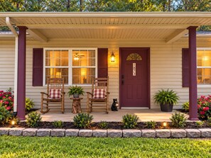 A house with a porch, two rocking chairs, a potted plant, a door with a number, and a small garden. - WOW 🤩 3BR Cabin just 2 miles to Dollywood + Arcades! (Sevierville)
