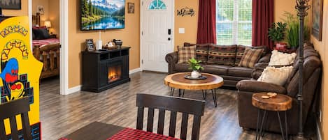 A cozy living room with a fireplace, a sofa, a coffee table, and a dining area with a checkered tablecloth.