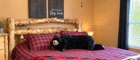 A bed with a wooden frame, a red and black checkered blanket, and two pillows.