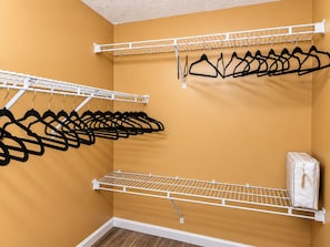 A closet with multiple white metal shelves and black hangers.