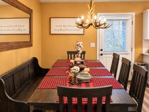 A dining room with a wooden table set for four, red and black checkered placemats, a chandelier, and framed quotes on the walls. - WOW 🤩 3BR Cabin just 2 miles to Dollywood + Arcades! (Sevierville)