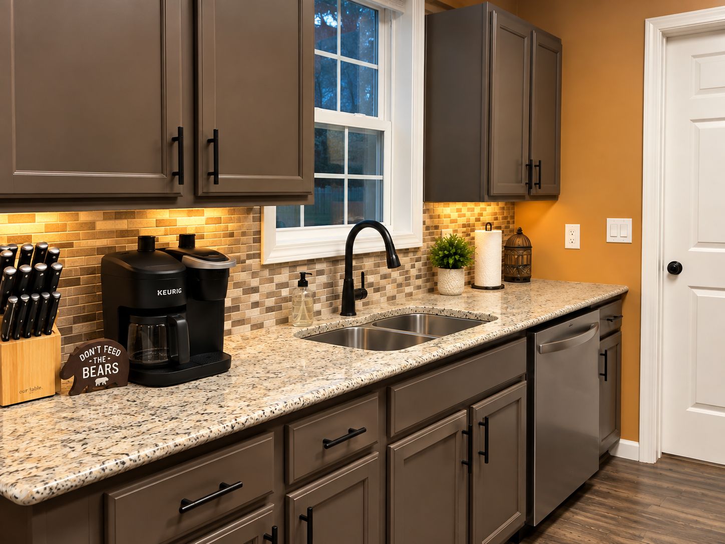 A kitchen with a granite countertop, stainless steel sink, and dark brown cabinets.