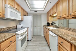 A compact kitchen with wooden cabinets, a microwave, a refrigerator, a dishwasher, and a skylight.