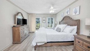 A bedroom with a bed, a dresser, a TV, and a balcony view. - Spacious and Oceanfront! (Saint Simons Island)