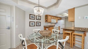 A modern kitchen with a glass dining table, white chairs, wooden cabinets, and a chandelier. - Spacious and Oceanfront! (Saint Simons Island)