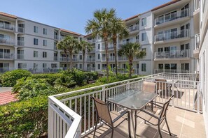 A multi-story residential building with balconies, palm trees, and a patio area with a table and chairs. - Spacious and Oceanfront! (Saint Simons Island)
