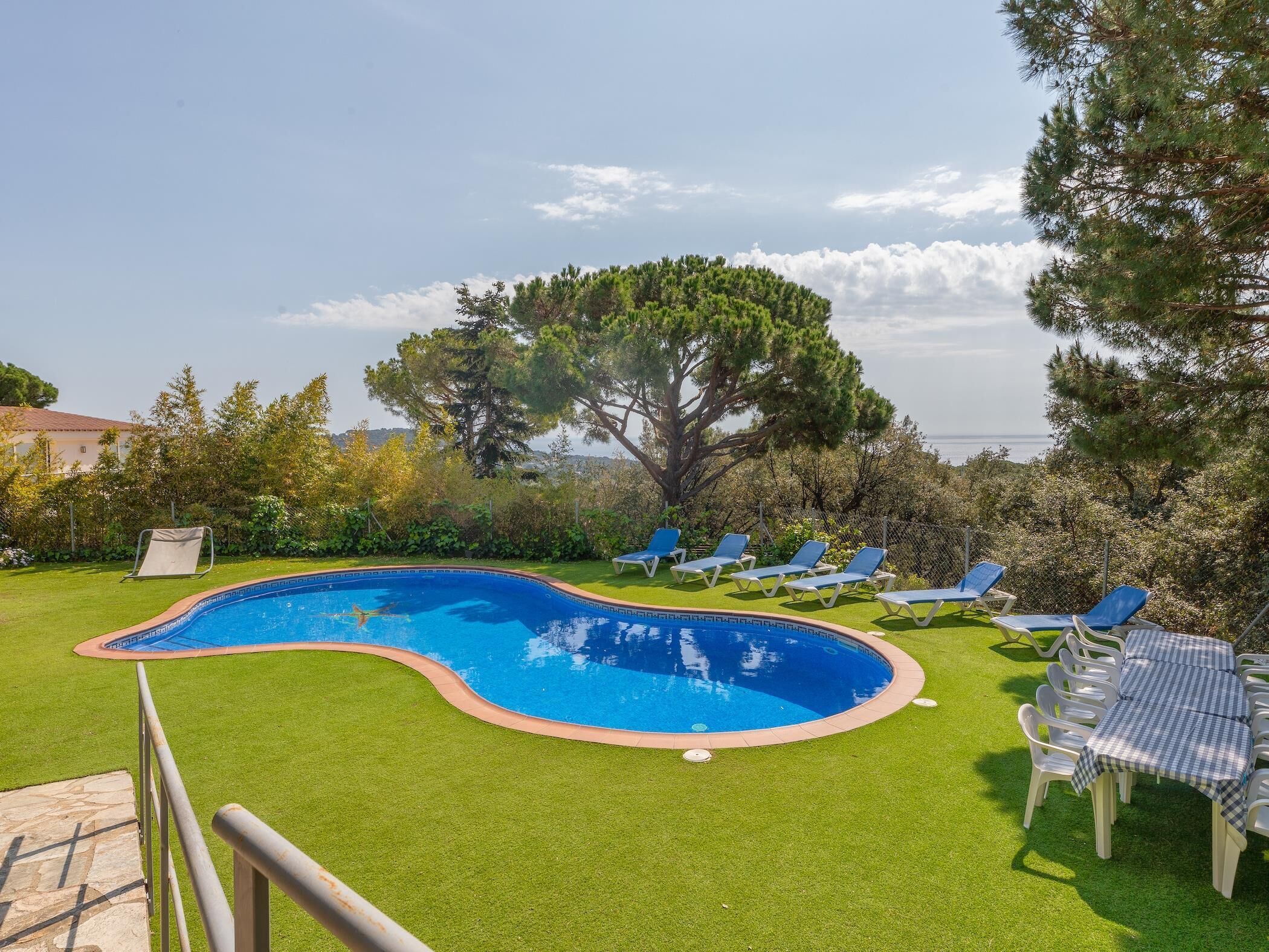 Une piscine à bord incurvé, entourée d’une pelouse bien entretenue et de plusieurs chaises longues.