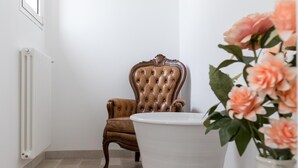 Une pièce avec un radiateur, un grand vase blanc rempli de fleurs et un fauteuil en cuir marron.