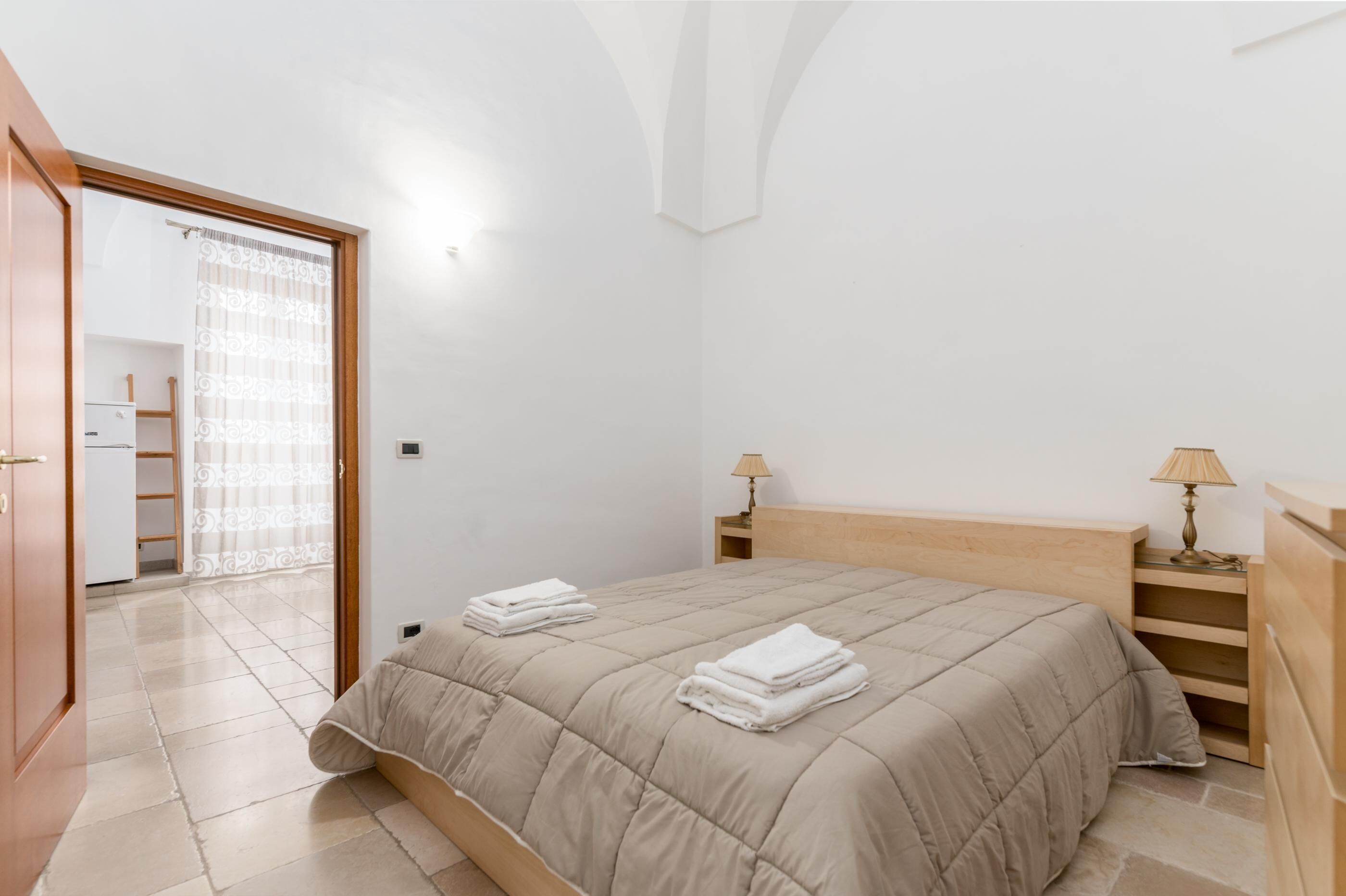 Un dormitorio con una cama, dos mesitas de noche, un cabecero de madera y una puerta que da a un baño.