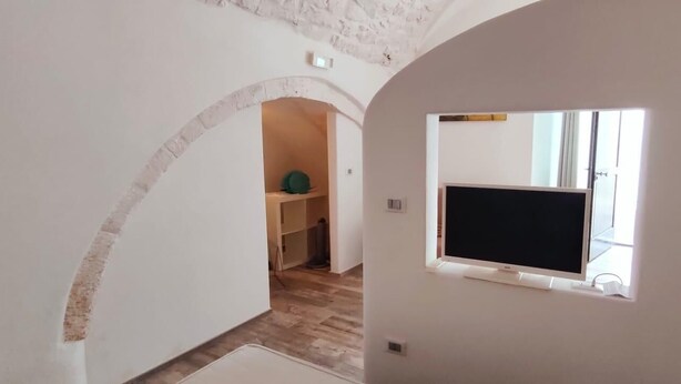 A room with a TV on a stand, a small window, and an arched doorway leading to another room. - La Maison Petite, Le Piccole Case Bianche (Ostuni)