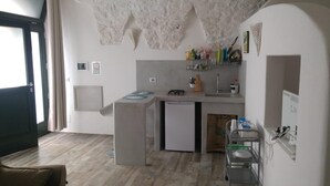 A compact kitchen with a small island, a built-in dishwasher, and a sink. There are various kitchen utensils and appliances on the countertops. - La Maison Petite, Le Piccole Case Bianche (Ostuni)