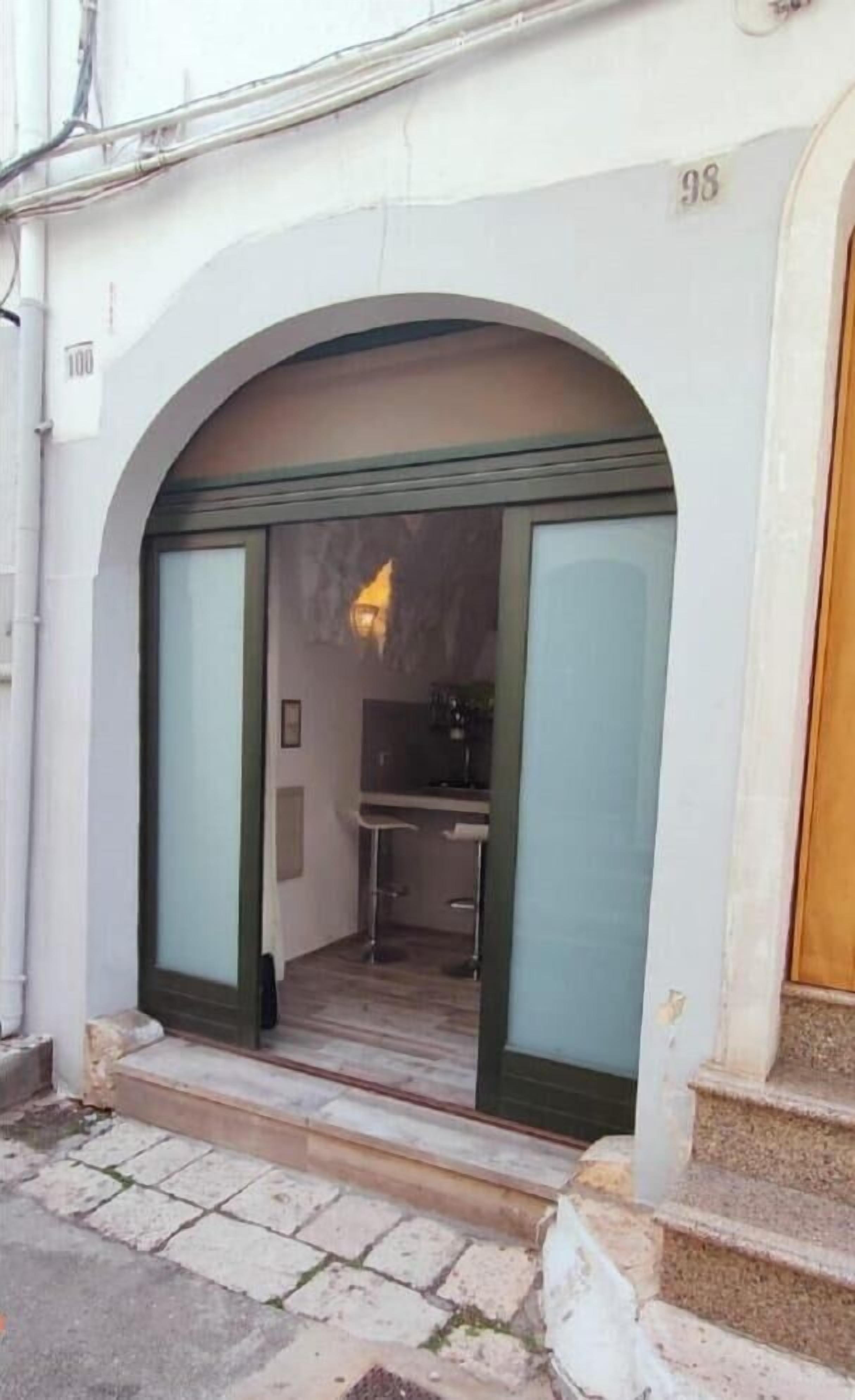 Une entrée d’immeuble avec une grande porte cintrée, une petite marche menant à cette porte, et le chiffre « 98 » au-dessus.