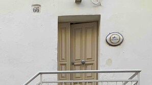 A building facade with a beige door, a metal railing with a diamond pattern, and a small plaque with the text "Blancostum". - biancostuni66, Le Piccole Case Bianche (Ostuni)