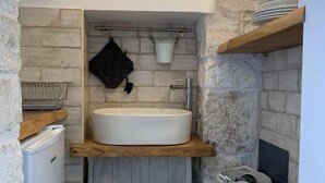 A compact kitchen with a built-in sink, a hanging pot rack, and a stone accent wall. - biancostuni66, Le Piccole Case Bianche (Ostuni)