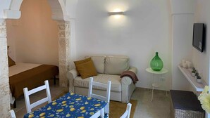 A cozy room with a sofa, a small table, and a television mounted on the wall. - biancostuni66, Le Piccole Case Bianche (Ostuni)