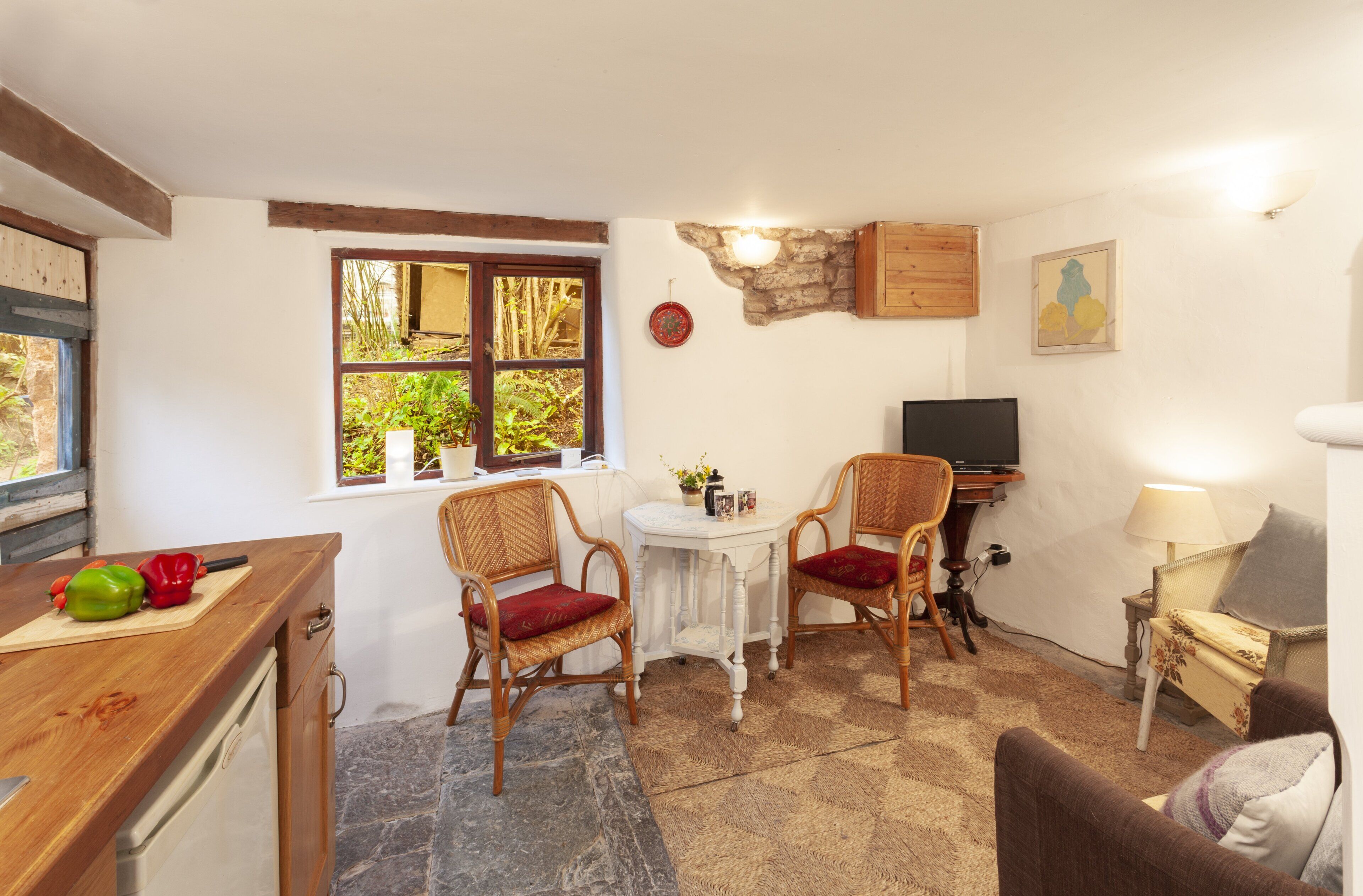 A cozy room with a kitchen area, two chairs, a small table, a television, and a lamp.