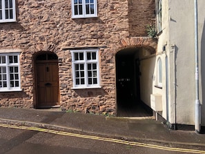 A stone building with a wooden door and two windows with white frames.