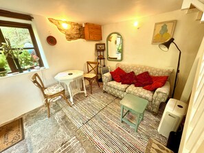 A cozy room with a patterned rug, a wooden chair, a small table, a sofa with red cushions, a radiator, and a lamp.