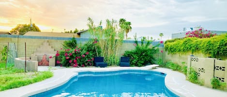 A swimming pool with a curved edge, surrounded by a concrete deck and a low stone wall.