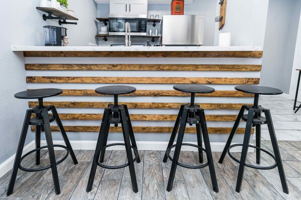 A kitchen with a white countertop, wooden steps, and four black stools.