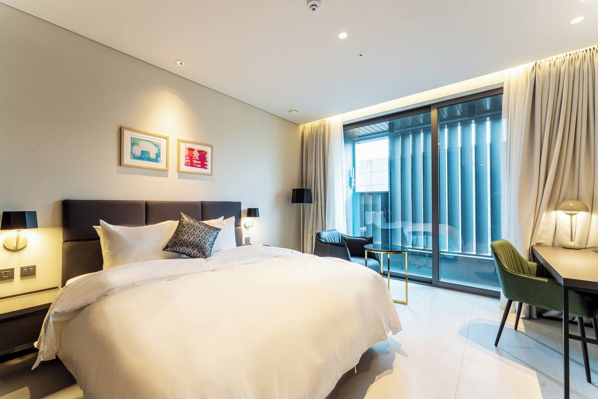 A modern hotel room with a large bed, a desk, and a balcony with curtains.