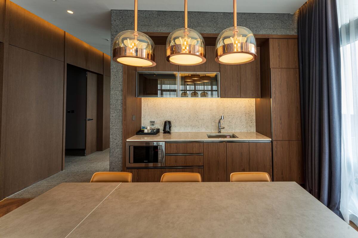A modern kitchen with a dining area, featuring a large island, built-in appliances, and pendant lighting.