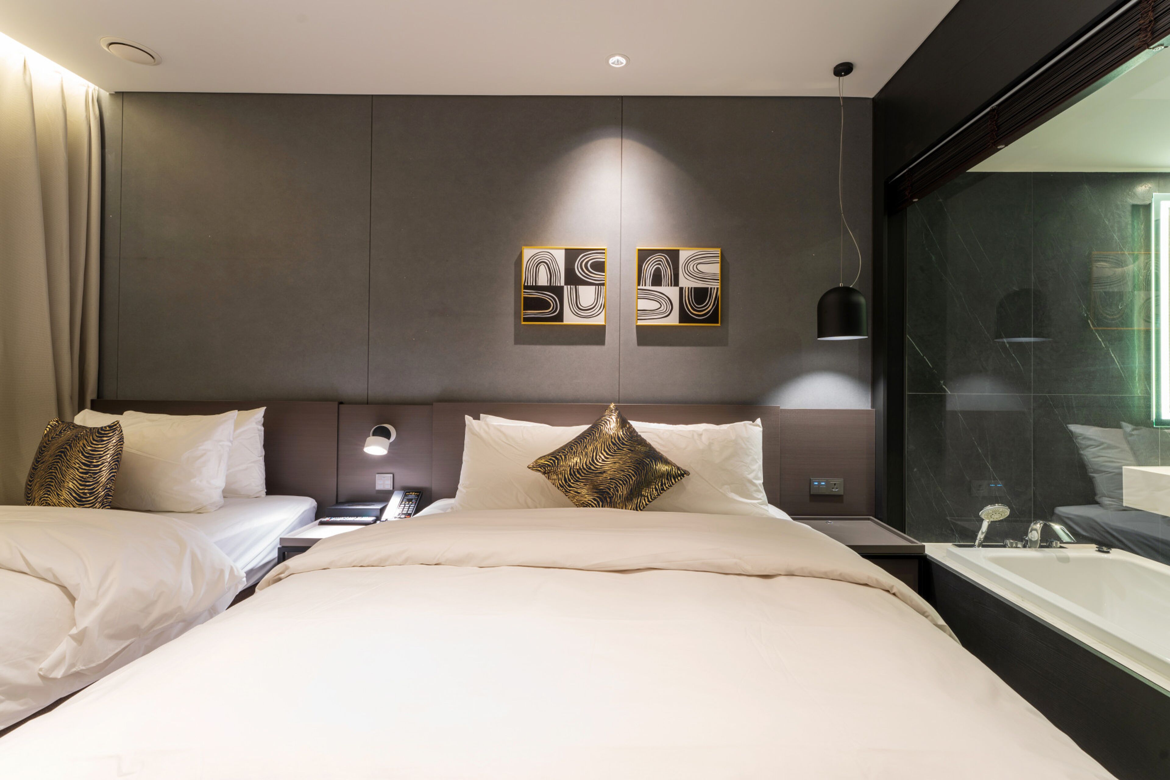 A hotel room with a large bed, a separate sofa bed, a bathroom with a bathtub, and artwork on the wall.