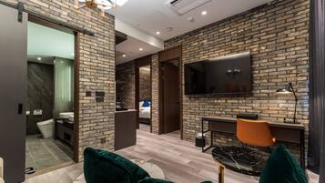 A modern hotel room with a brick wall, a flat-screen TV, a desk with a chair, and a large window.