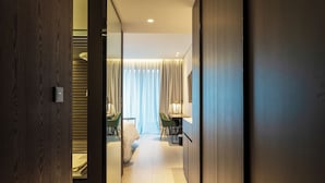 A hotel room with a wooden door, a bed with white linens, a desk with a chair, and a large window with curtains. - Hotel Soulhada (Incheon)