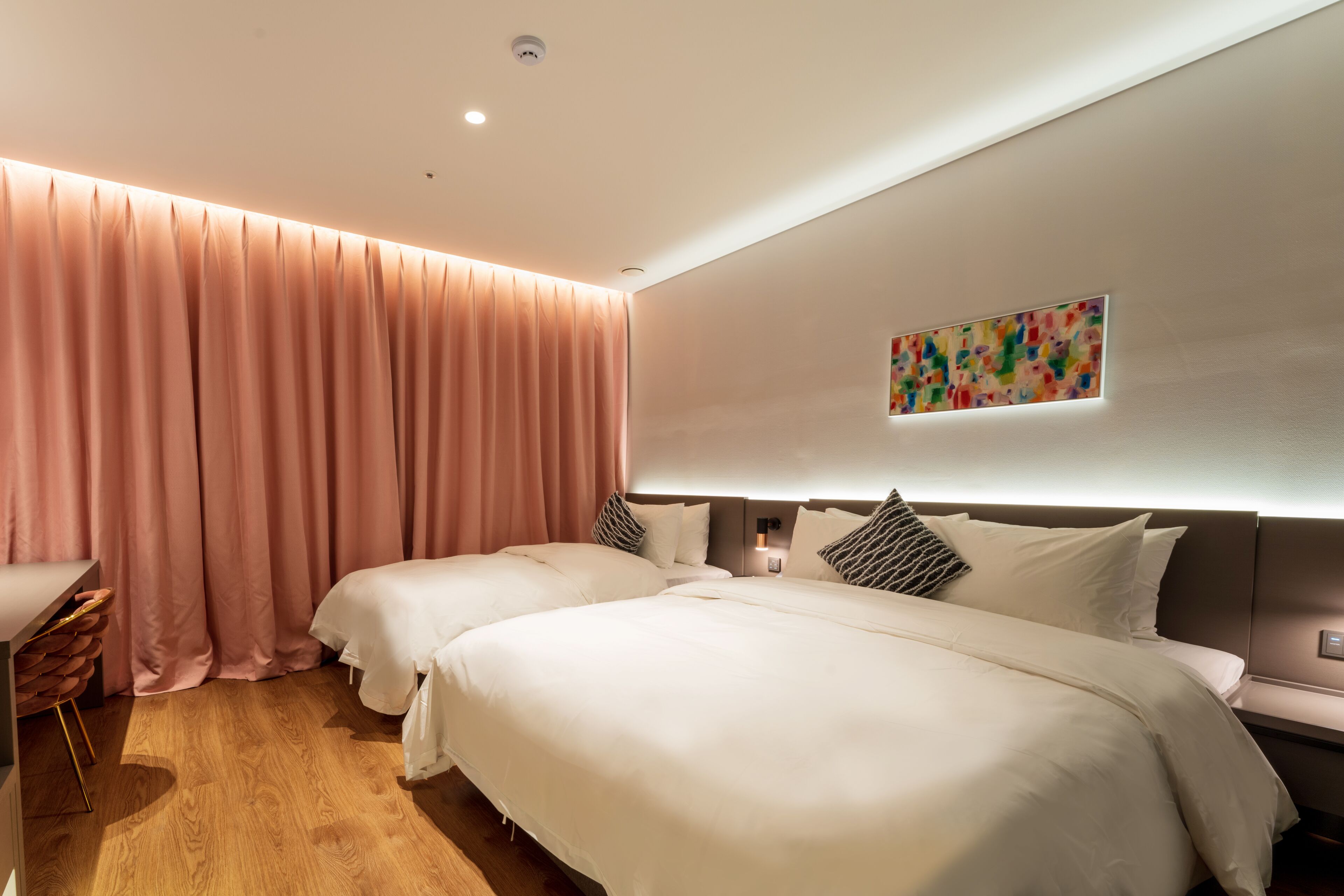 A hotel room with two beds, a desk, and a large window with curtains.