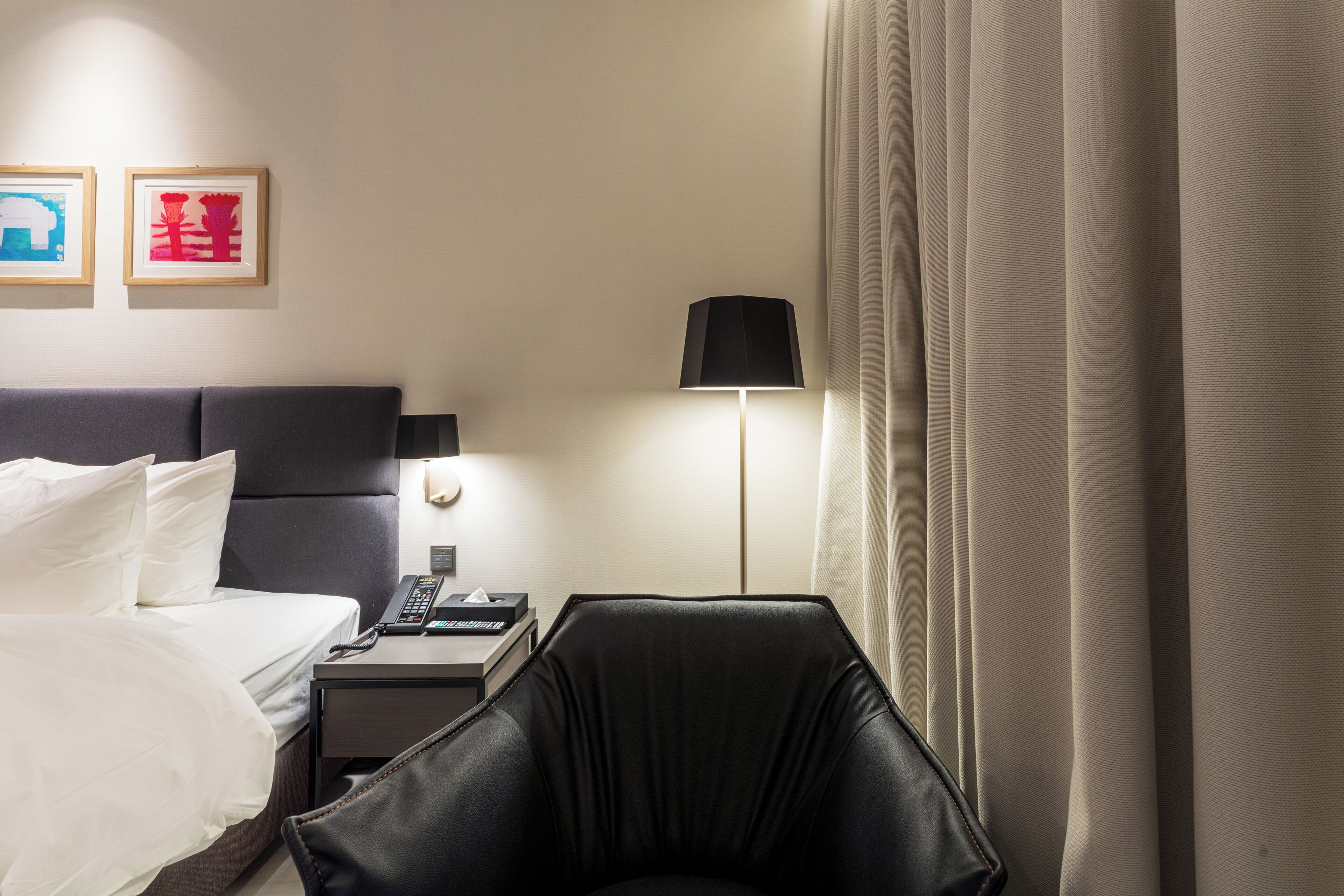 Hotelkamer met een bed, een bureau met een lamp, een stoel en twee afbeeldingen in lijsten aan de muur.