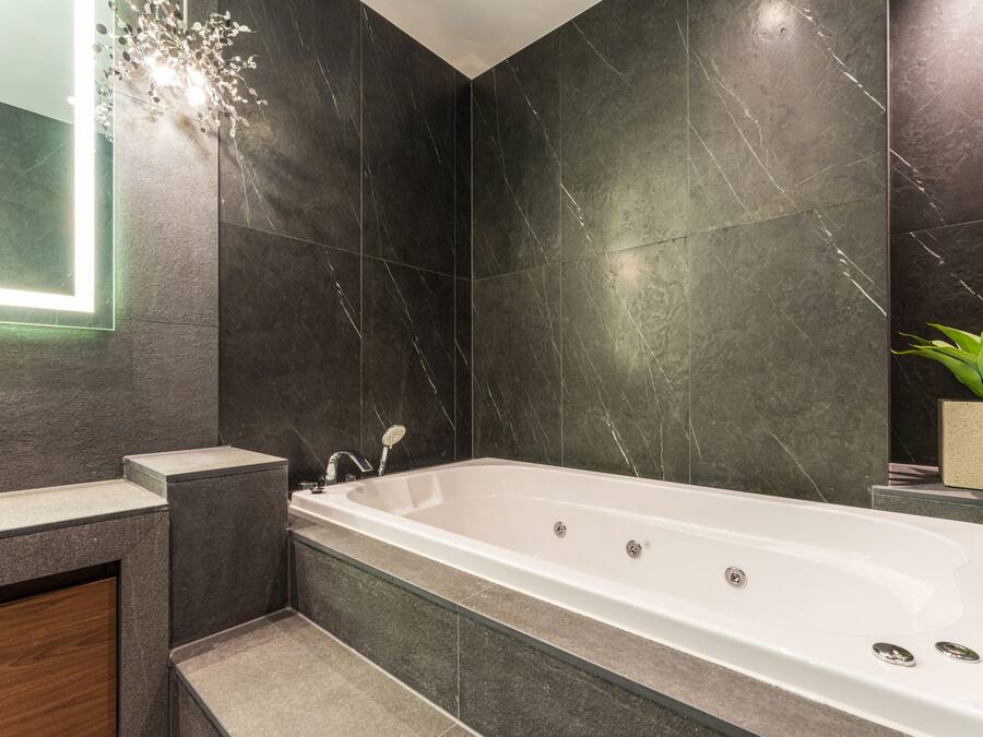 Un baño moderno con una bañera independiente, paredes de mármol oscuro y una pequeña planta en maceta.