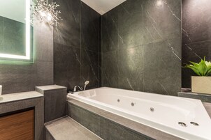 A modern bathroom with a freestanding bathtub, dark marble walls, and a small potted plant.