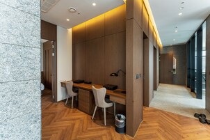 A modern hotel room with a wooden desk, two chairs, a small trash bin, and a pair of shoes on the floor.
