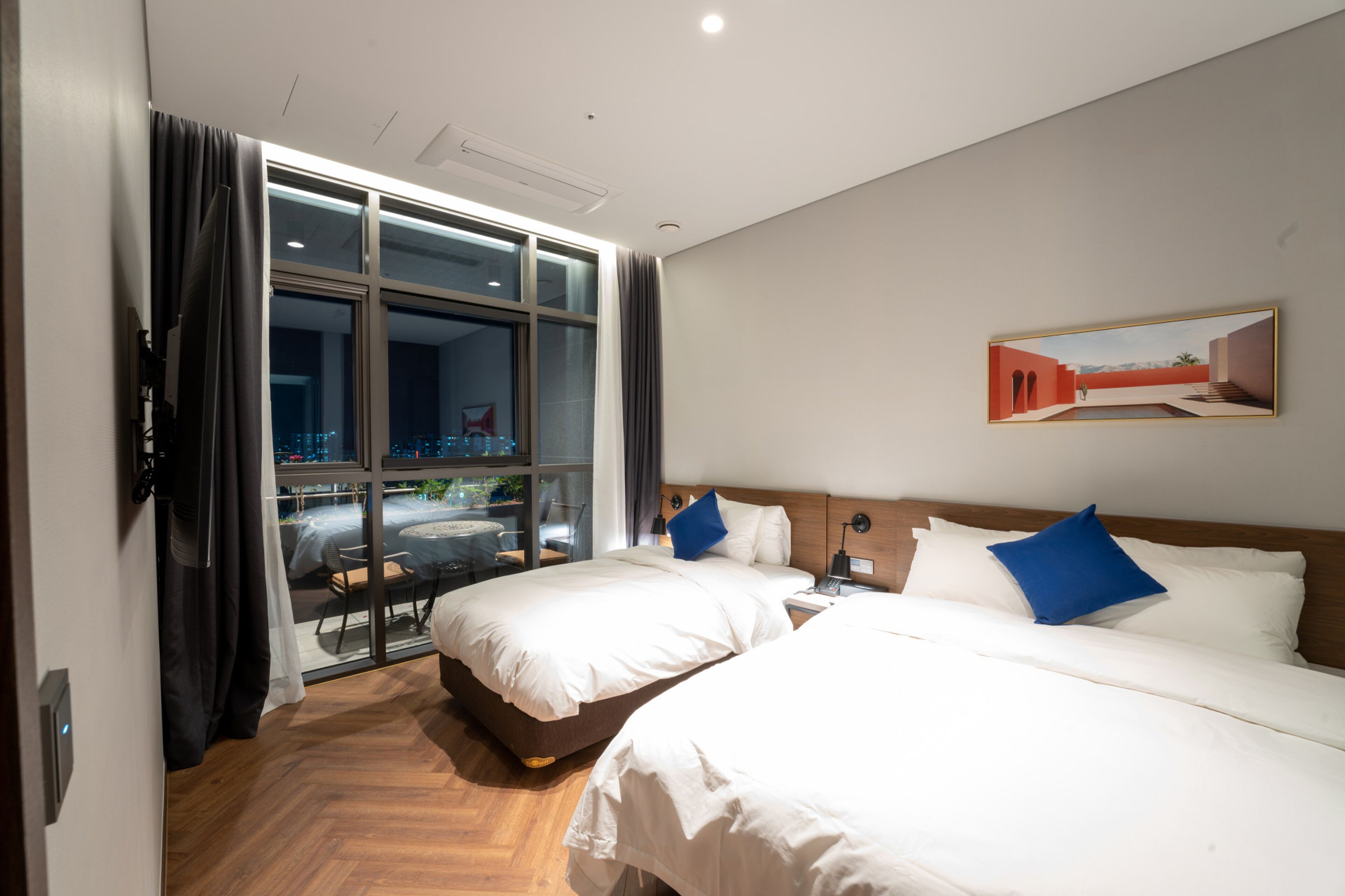 A hotel room with two beds, a large window, and a painting on the wall.