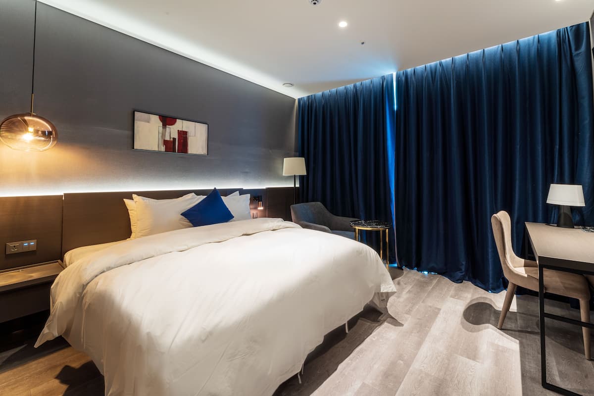 A modern hotel room with a large bed, a desk, and a chair.