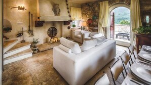 Ein gemütliches Wohnzimmer mit einem weißen Sofa, Steinwänden und Blick ins Freie durch ein großes Fenster.